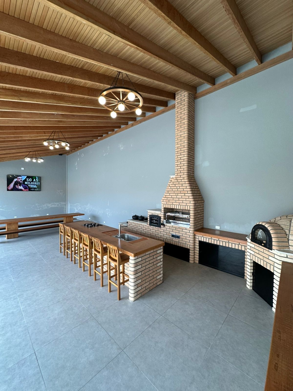 Área gourmet com churrasqueira, forno e mesas de madeira