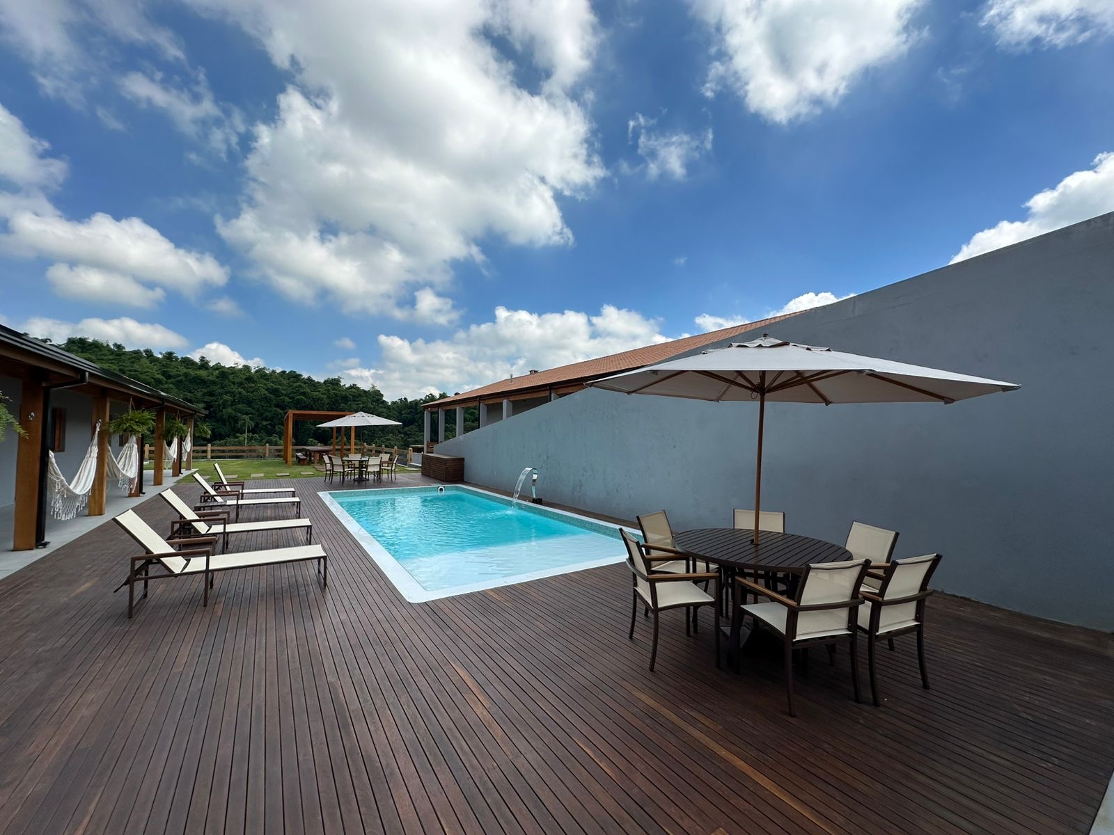 Deck de madeira com espreguiçadeiras e mesa sob ombrelone