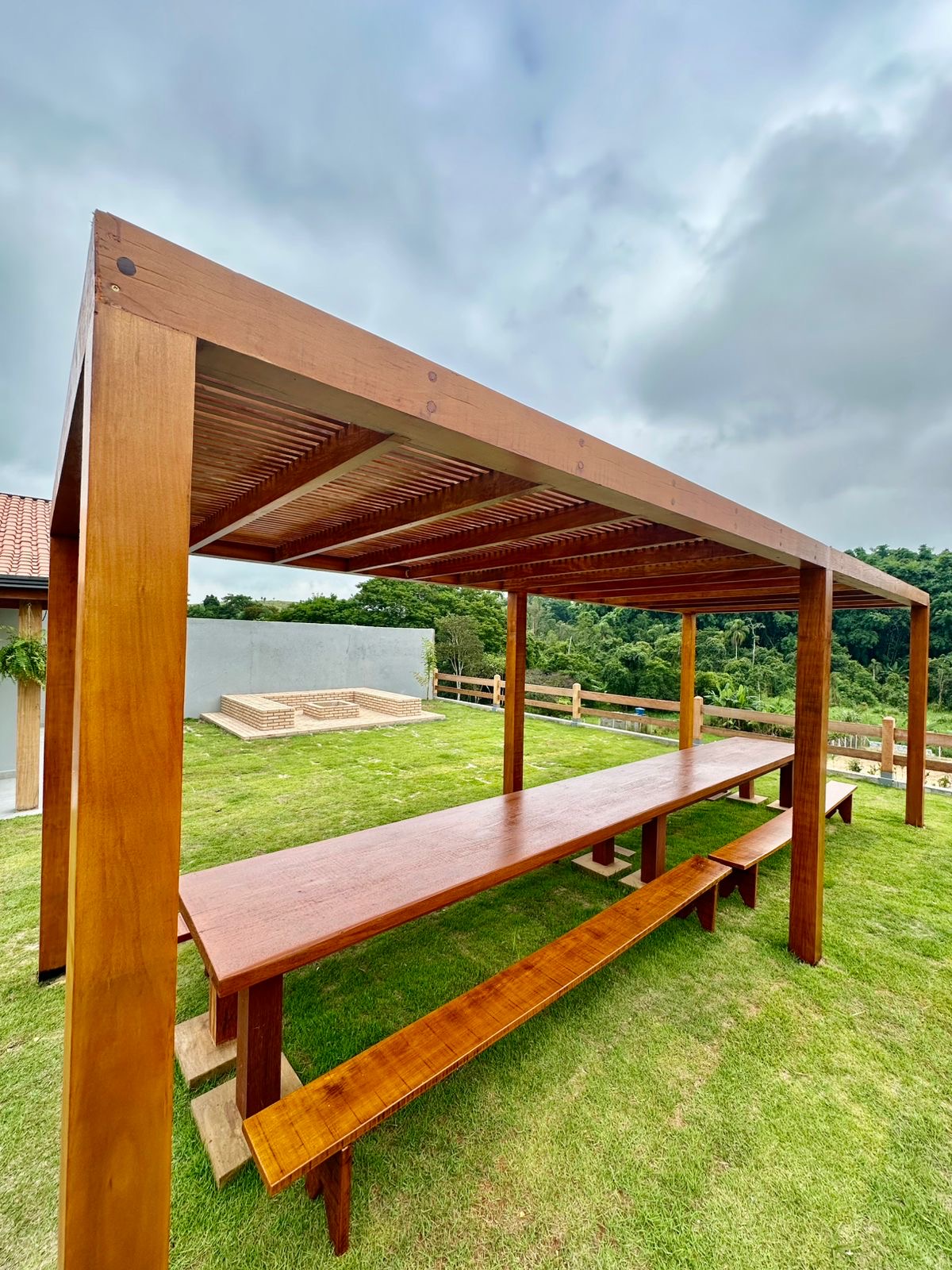 Pergolado de madeira com mesa longa e vista para o fogo de chão